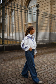 Chemise brodée à col montant portée par une femme, en marchant, grille, pavés