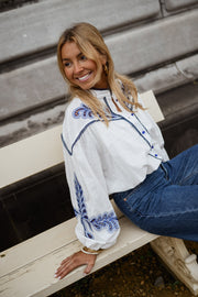 Chemise brodée à col montant portée par une femme, assise, banc, sourire