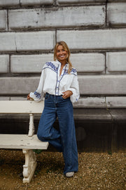 Chemise brodée à col montant portée par une femme, vue de face, banc, jean large