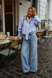 Chemise rayée à cravate portée par une femme, silhouette entière, jean large, foulard noué au cou