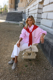 Chemise rayée à revers amovible portée par une femme, assise, sur un banc, pull rouge sur les épaules