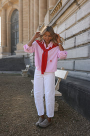 Chemise rayée à revers amovible portée par une femme, silhouette entière, pull rouge sur les épaules, pantalon blanc