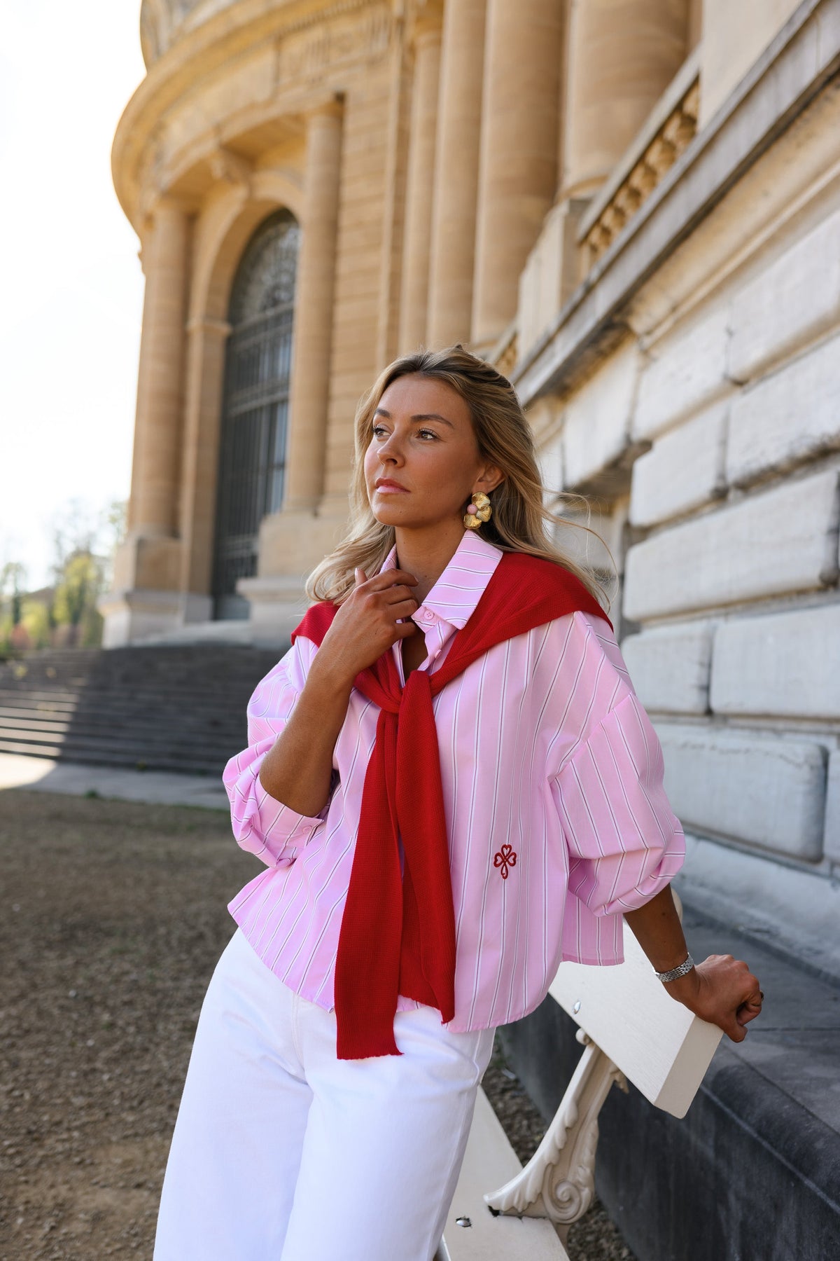 Chemise rayée à revers amovible portée par une femme, silhouette entière, pull rouge sur les épaules, banc