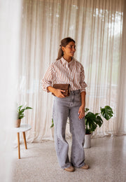 Chemise rayée boutonnée portée par une femme, silhouette entière, rideaux, sac