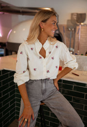 Chemise fleurie à manches longues portée par une femme, vue de face, comptoir carrelé, jean gris