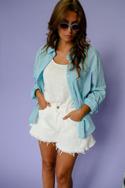 Chemise à carreaux à épaulettes turquoise portée par une femme, vue rapprochée, lunettes de soleil, mains dans les poches