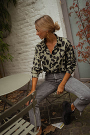 Chemise léopard légèrement ample portée par une femme, assise, chaise, jean