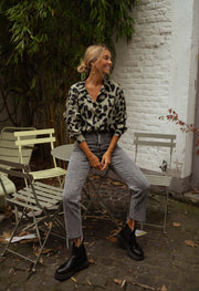 Chemise léopard légèrement ample portée par une femme, assise, chaise pliante, bottines