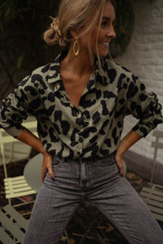 Chemise léopard légèrement ample portée par une femme, vue de face, jean gris, mur blanc