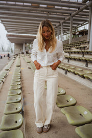 Chemise brodée à marguerites blanche portée par une femme, vue de face, gradins, pantalon écru