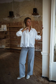 Chemise courte à dentelle portée par une femme, vue de face, mur en briques, jean large