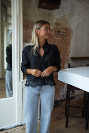 Chemise à dentelle transparente portée par une femme, vue de face, mur en briques, jean clair