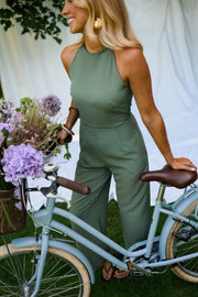 Combinaison longue dos ouvert kaki portée par une femme, vue de trois-quarts, vélo bleu, fleurs