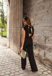 Combinaison fluide dos ouvert portée par une femme, vue de face, porte en bois, pochette