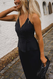 Combinaison longue dos ouvert noire portée par une femme, vue de trois-quarts, pochette noire, main dans les cheveux