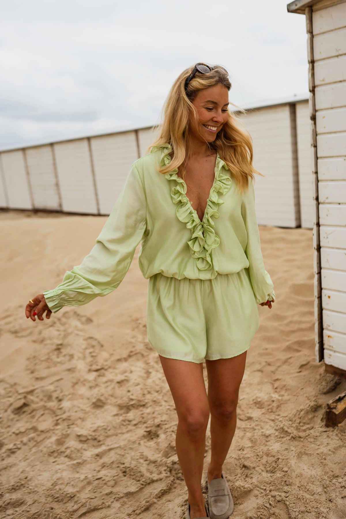 Combishort à volants boutonné porté par une femme, silhouette entière, sable, cabine de plage