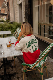 Gilet torsadé à poches porté par une femme, assise, terrasse, chaise rayée vert