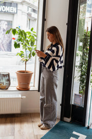Pull rayé à col zippé porté par une femme, silhouette entière, plante, porte vitrée