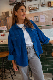 Surchemise loose en velours bleue portée par une femme, vue de face, comptoir carrelé, sourire