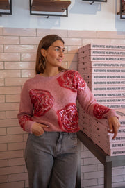 Pull doux à paillettes framboise porté par une femme, vue de face, mur rose, jean