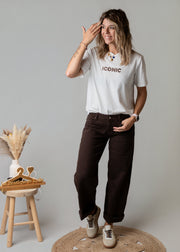 Pantalon coupe barrel en sergé porté par une femme, vue de trois-quarts, t-shirt blanc, tabouret
