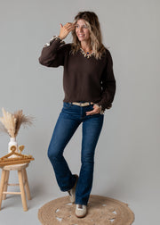 Pull col V léopard porté par une femme, vue de trois-quarts, main sur le visage, jean flare