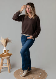 Pull col V léopard porté par une femme, silhouette entière, jean flare, tabouret