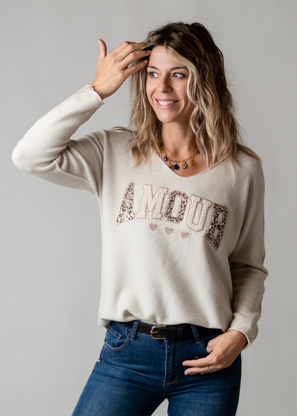 Pull brodé en maille fine porté par une femme, vue de trois-quarts, lettrage, main sur la tête