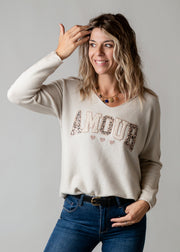 Pull brodé en maille fine porté par une femme, vue de trois-quarts, lettrage, main sur la tête