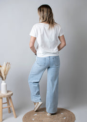 Jean large taille haute stretch porté par une femme, vue de dos, t-shirt blanc, tabouret