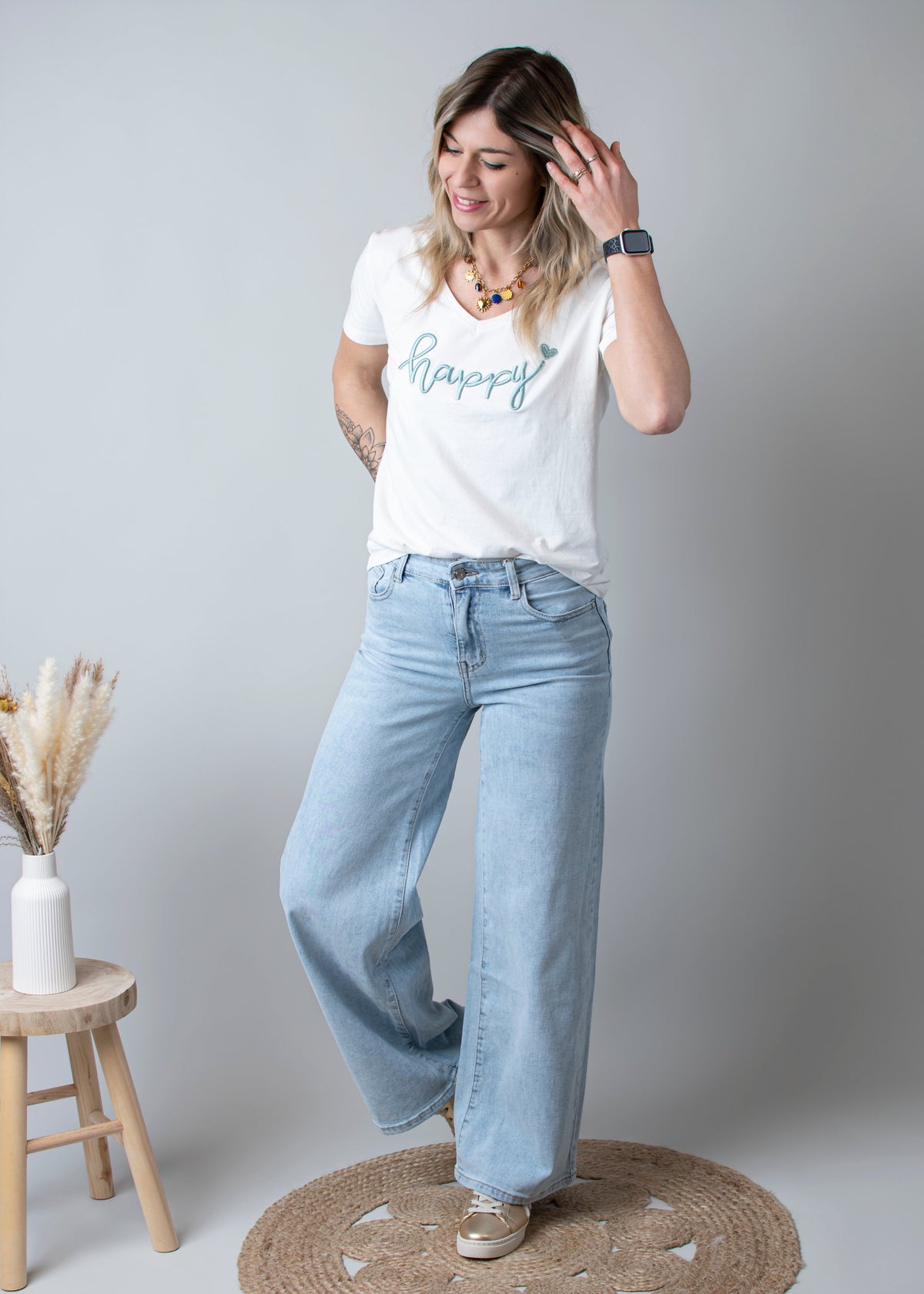 Jean large taille haute stretch porté par une femme, silhouette entière, t-shirt blanc, tabouret