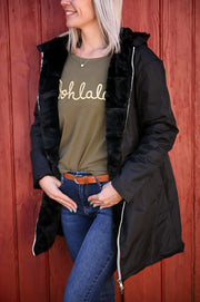 Parka réversible à fourrure portée par une femme, vue de trois-quarts, mur rouge, parka noire