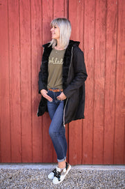 Parka réversible à fourrure portée par une femme, silhouette entière, mur rouge, baskets