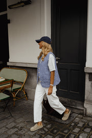 Gilet vichy sans manches porté par une femme, en marchant, casquette, porte noire