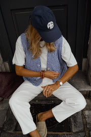 Gilet vichy sans manches porté par une femme, assise, casquette, jambes croisées