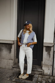 Gilet vichy sans manches porté par une femme, silhouette entière, casquette, pantalon blanc, de loin