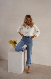 Gilet à boutons fleuris écru porté par une femme, silhouette entière, jean, cube blanc, mimosa