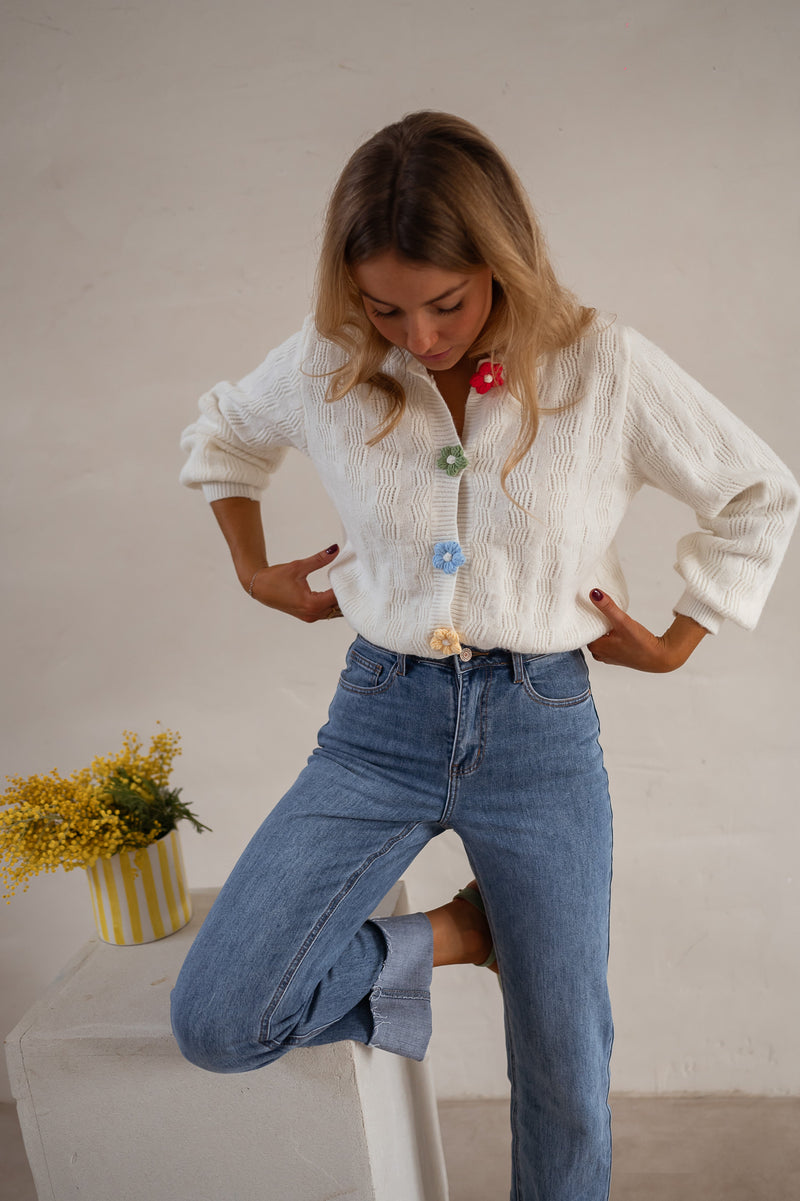 Gilet à boutons fleuris écru porté par une femme, vue rapprochée, boutons en forme de fleurs, mains sur les hanches