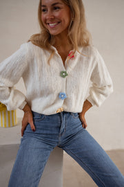 Gilet à boutons fleuris écru porté par une femme, vue rapprochée, boutons fleurs, sourire