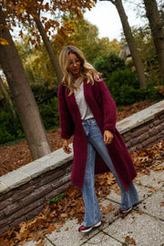 Gilet long à poches bordeaux porté par une femme, vue de trois-quarts, feuilles d'automne, jambe croisée