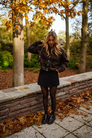 Gilet rayé col rond marron porté par une femme, vue de face, muret en pierre, feuilles d'automne