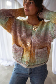 Gilet en maille tie-dye porté par une femme, assise, jambe croisée, jean bleu