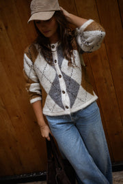 Gilet jacquard à col rond porté par une femme, vue de trois-quarts, mur en bois, jean bleu