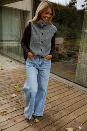 Gilet sans manches boutonné gris porté par une femme, en marchant, terrasse en bois, mains dans les poches