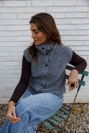Gilet sans manches boutonné gris porté par une femme, vue de trois-quarts, mur blanc, cheveux bruns