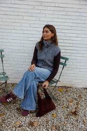 Gilet sans manches boutonné gris porté par une femme, assise, chaise verte, sac bordeaux