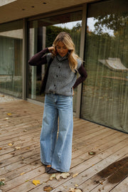 Gilet sans manches boutonné gris porté par une femme, vue de trois-quarts, terrasse en bois, jean large