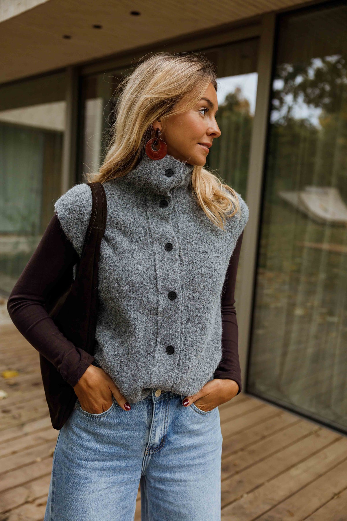 Gilet sans manches boutonné gris porté par une femme, vue de face, terrasse en bois, jean bleu