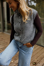 Gilet sans manches boutonné gris porté par une femme, vue de trois-quarts, jean bleu, sourire