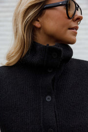 Gilet sans manches boutonné noir porté par une femme, vue rapprochée, col montant, boutons